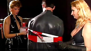 Two masked latex chicks jerk off his hard cock
